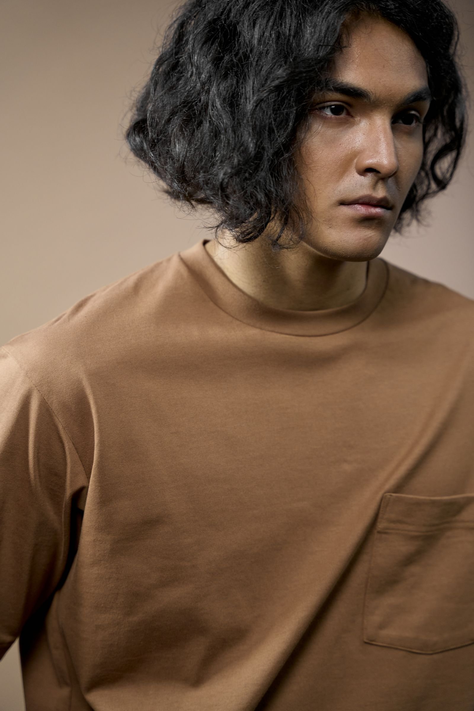 Homem com camiseta marrom de gola redonda e bolso na frente