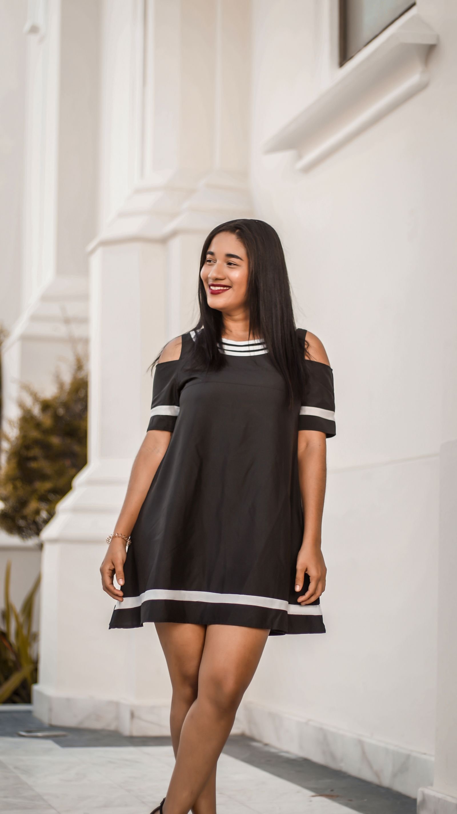 Mulher com vestido preto e faixas claras na gola, nas mangas e na barra